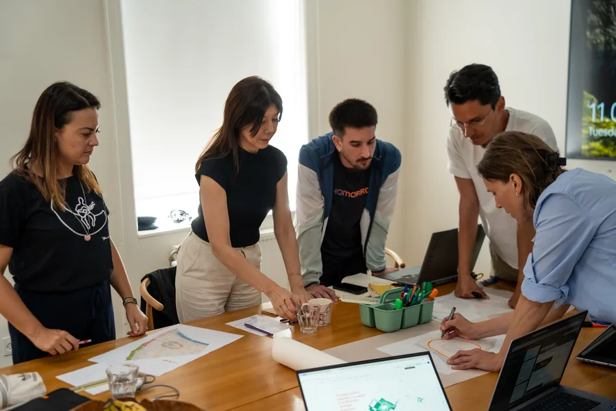 Três pessoas analisando uma maquete sobre a mesa